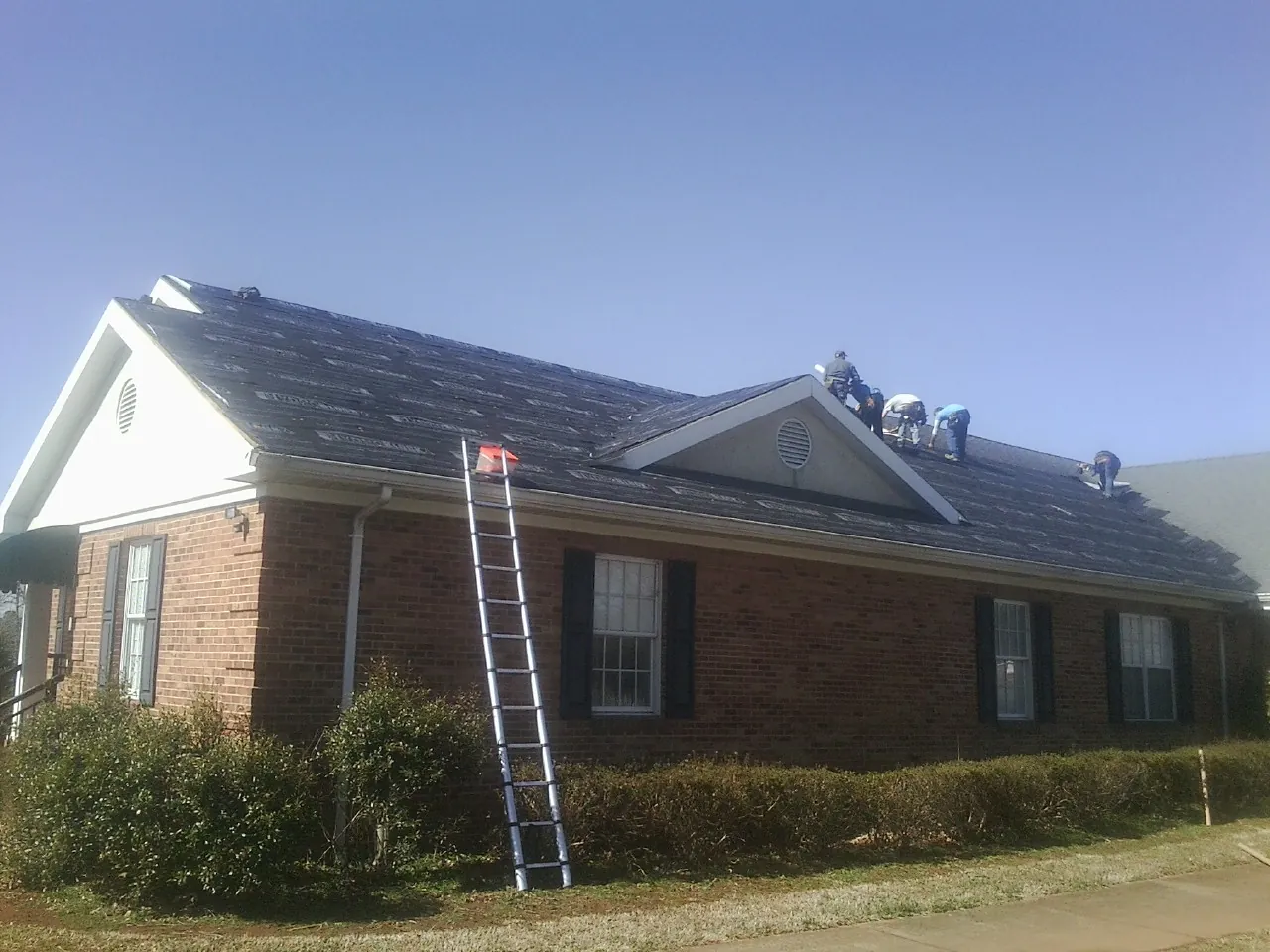 Crew tearing shingles off a brick ranch roof with a ladder set — Emergency Roof Repair work by our crew in Sycamore