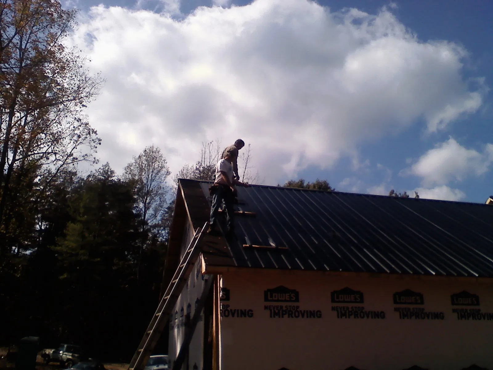 Roofer fastening dark metal panels high against a cloudy sky, from a Roof Inspection job in Sycamore