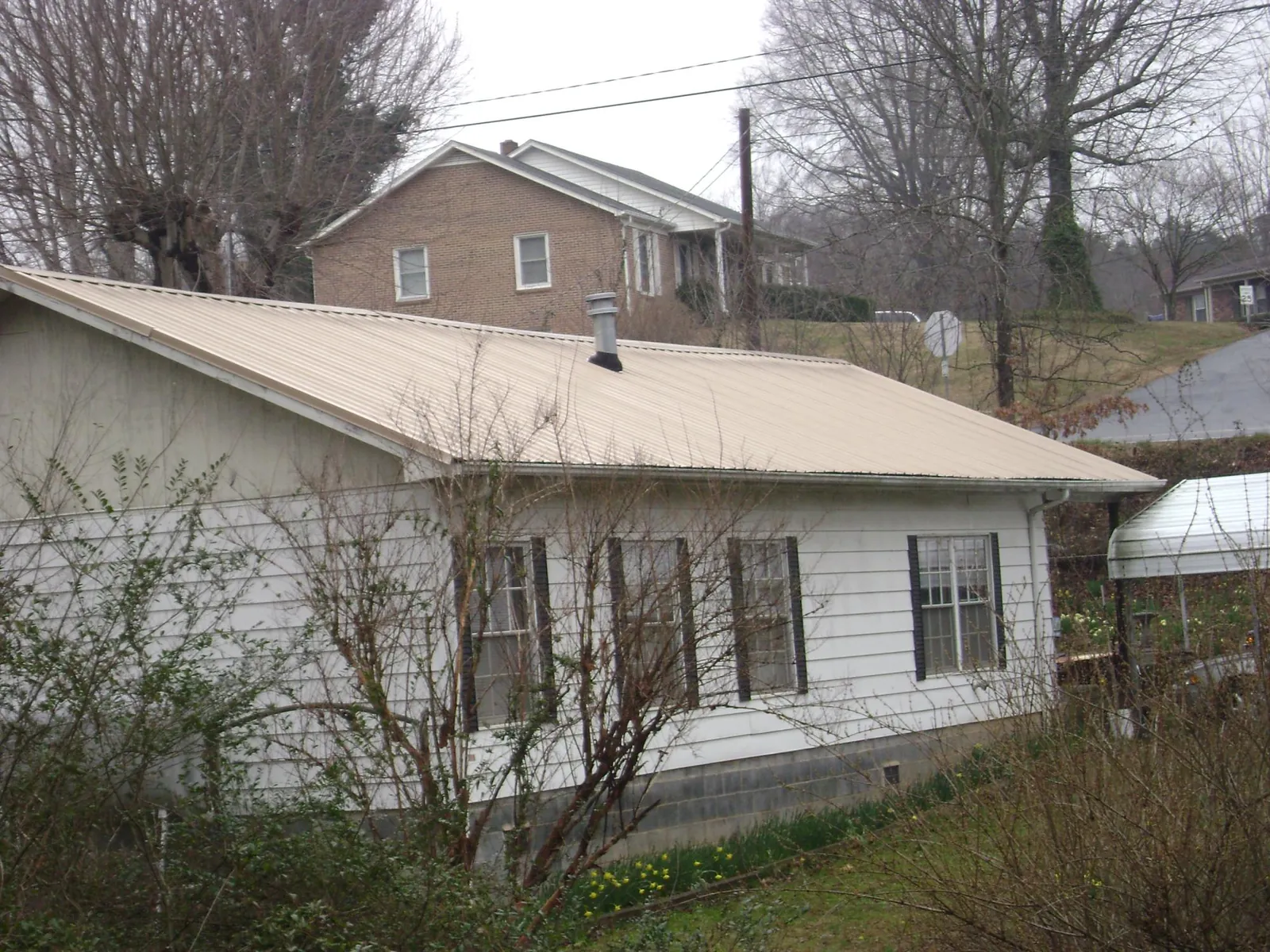 Tan metal roof on a white sided house set into a hillside — Commercial Roofing by Roofing Brothers in Sycamore